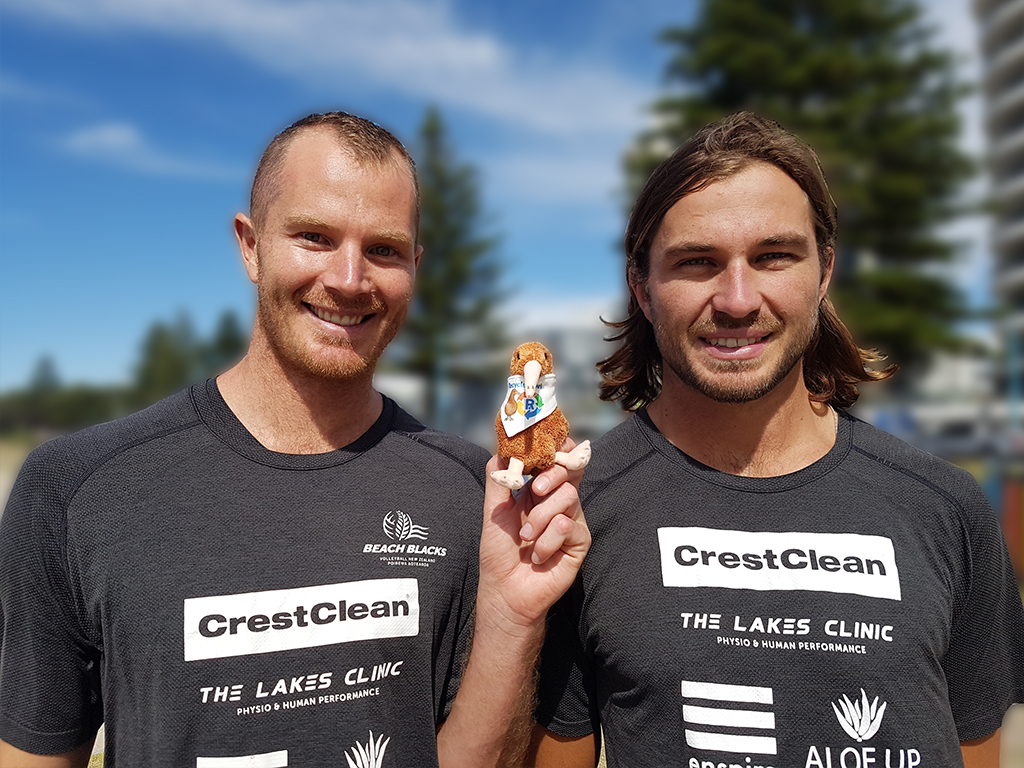 Beach volleyballers holding kiwi mascot.